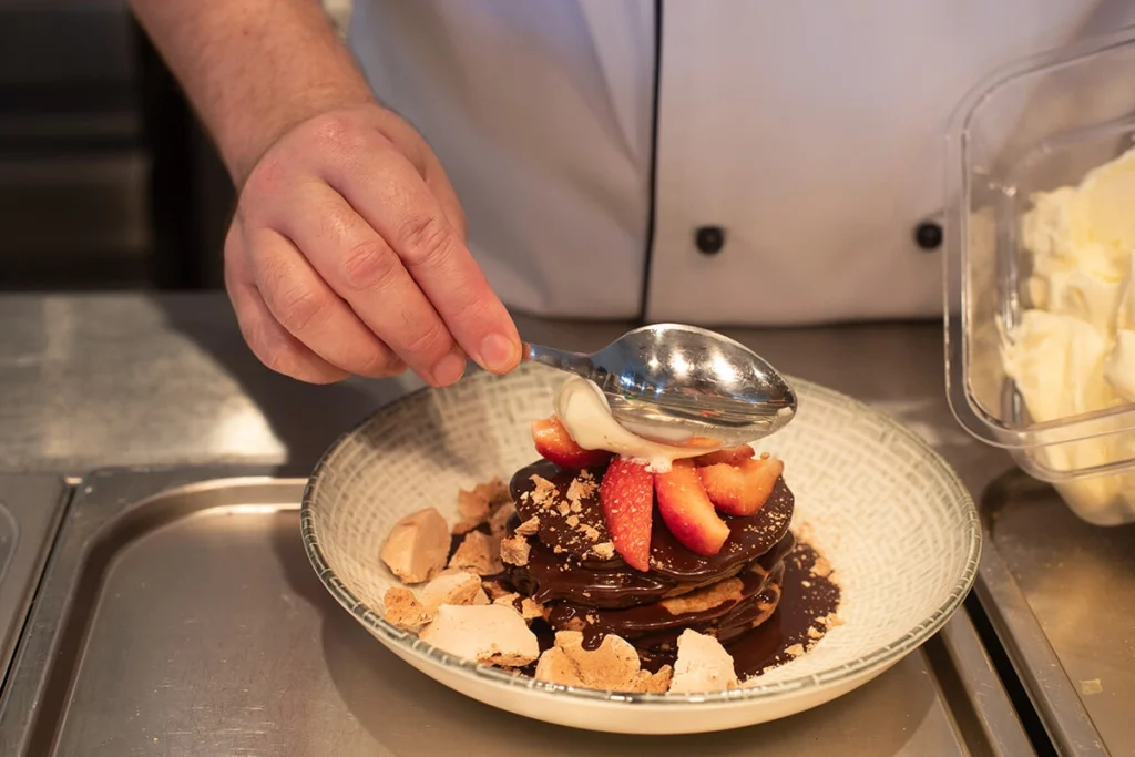 Image of chef hand plating pancakes with cream